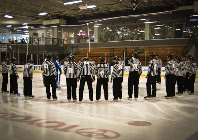 National Hockey League referees gather students in a huddle to teach them how to be better hockey officials. 