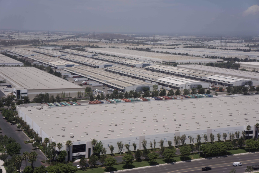 An aerial view of the roofs of vast grey warehouses, stretching far into the horizon