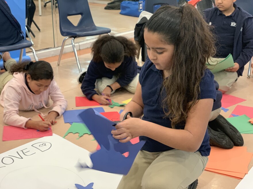 A KIPP Philosophers Academy student cuts out paper butterflies in rainbow colors as part of a sign that says, "You Are Loved."