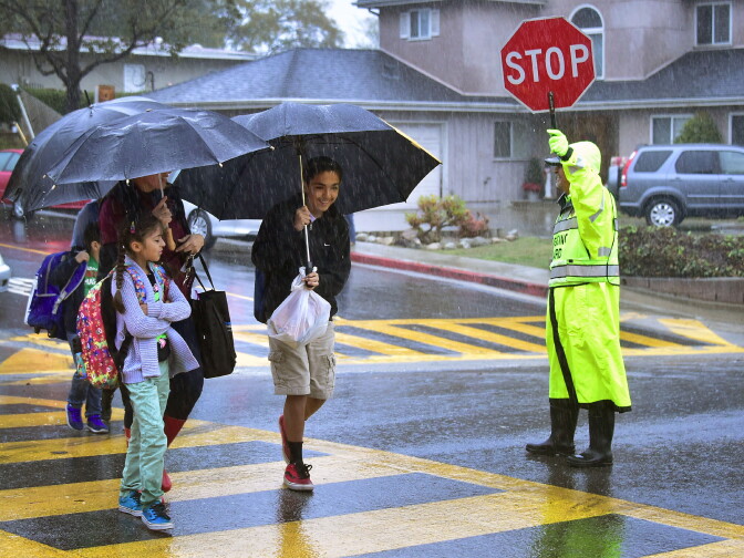 A school crossing guard holds up a sign to stop traffic as students and parents walk in the rain on Dec. 16, 2016 in Monterey Park as the biggest rain storm of the season hits Southern California.
