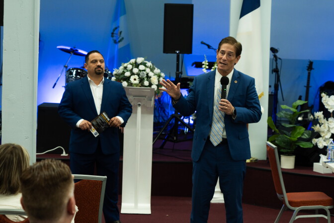 A man with a microphone speaks in a church building to a crowd.