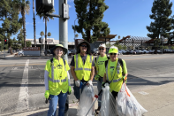 Four Volunteers Cleaning Communities members stand together for a picture. They all wear hats and neon yellow clothing. Three of them are holding trash bags.