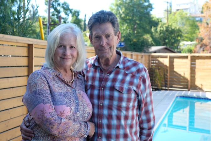 A white woman with light hair and a white man with gray hair stand near a pool.