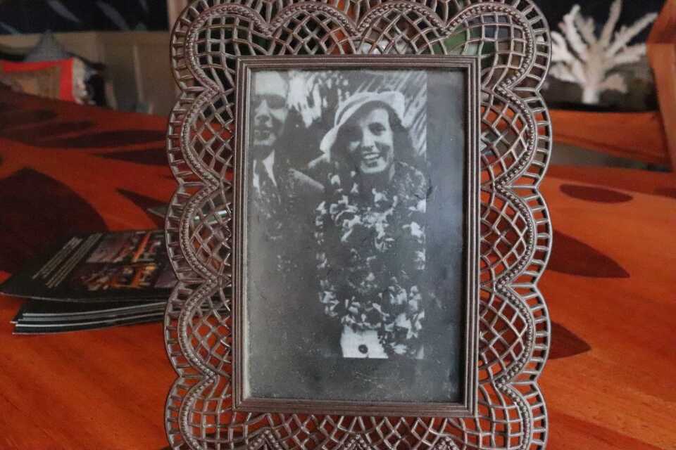 A framed black and white photo of a young man and woman. They are both smiling. The woman is wearing a sun hat and a pile of lei necklaces. The man wears a suit and tie. 