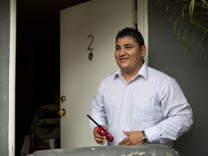 Los Angeles, CA: July 12, 2012 - Ronald Aldana stands near the front door of his home, watching for rain, before relighting the grill where he is in the process of cooking food for dinner for his girlfriend, her mother and friends.