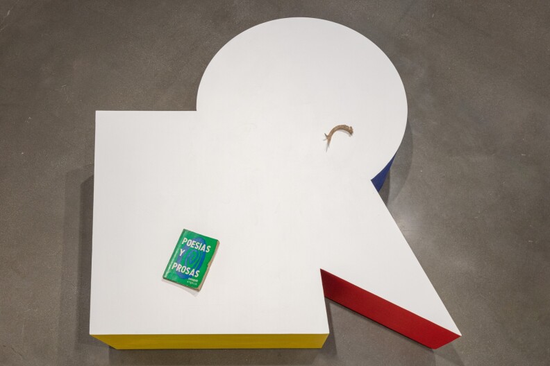 Una plataforma con tapa blanca, de forma geométrica inusual, con un asta de ciervo en la parte circular superior derecha, el Libro de Poesías y Prosas en la parte inferior izquierda del gran cuadrado de la estatua de la plataforma. A los lados se puede ver amarillo, rojo y azul.