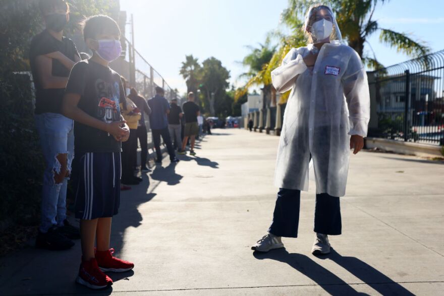 SAN FERNANDO, CALIFORNIA - DECEMBER 2: A USC research team member (R) recruits families to participate in a rapid antigen testing program as people wait in line at a walk-up COVID-19 testing site on December 2, 2020 in San Fernando, California. California reported 20,759 new coronavirus cases today, a one-day record for the state, amid a new limited stay-at-home order in Los Angeles County. (Photo by Mario Tama/Getty Images)