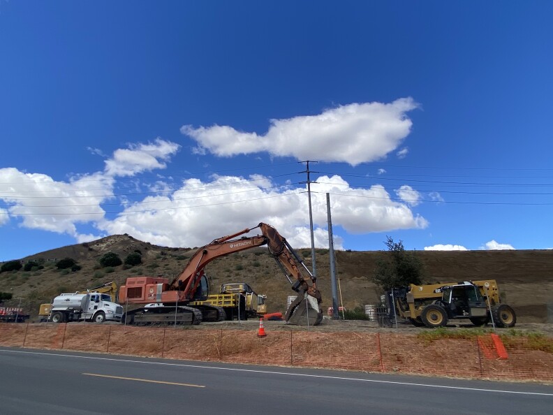 A bulldozer on the size of the road with fluffy clouds against a blue sky.