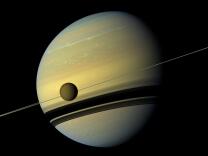 A giant of a moon appears before a giant of a planet undergoing seasonal changes in this natural color view of Titan and Saturn from NASA's Cassini spacecraft. Titan, Saturn's largest moon, measures 3,200 miles across and is larger than the planet Mercury. As the seasons have changed in the Saturnian system, and spring has come to the north and autumn to the south, the azure blue in the northern Saturnian hemisphere that greeted Cassini upon its arrival in 2004 is now fading. The southern hemisphere, in its approach to winter, is taking on a bluish hue. This mosaic combines six images — two each of red, green and blue spectral filters. The images were obtained by Cassini's wide-angle camera on May 6, 2012, at a distance of approximately 483,000 miles from Titan.

