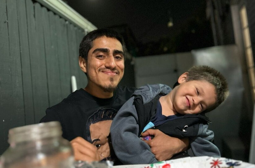 A young man with medium-toned skin smiles as he holds a squirming young boy in his arms at a dinner table. 