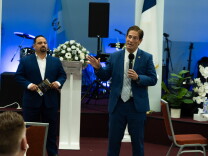 A man with a microphone speaks in a church building to a crowd.