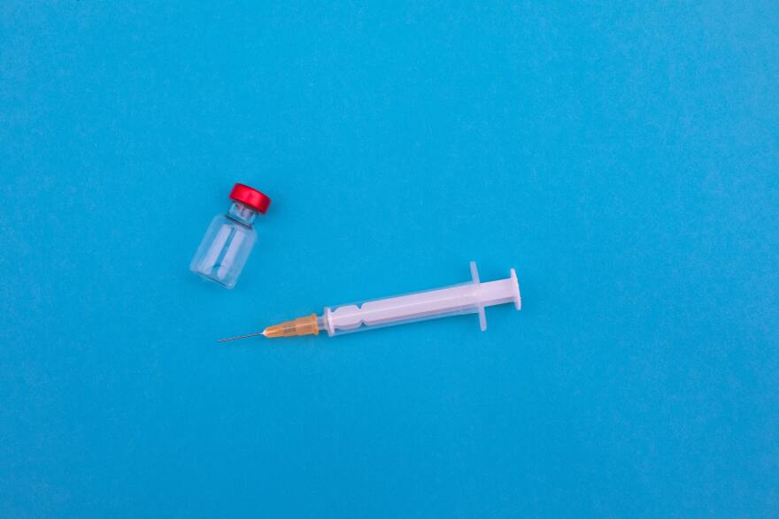 a clear vial with a red lid and a medical needle sit against a blue backgroudn