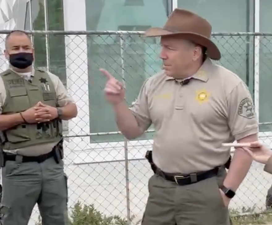 An image of Sheriff Alex Villanueva wearing a cowboy hat and gesturing with his index finger as he speaks near the Venice Boardwalk.