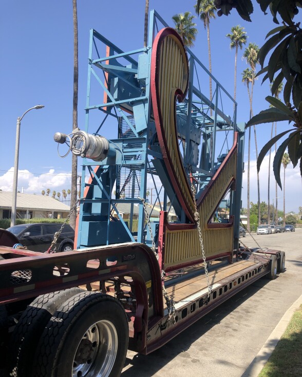 A giant neon sign of the letter "K" is placed horizontally on the flatbed of a giant truck