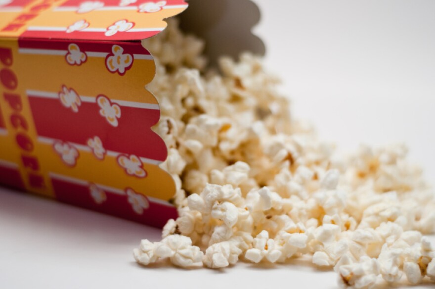 A box of movie popcorns is on it's side with the popcorn spilling out.