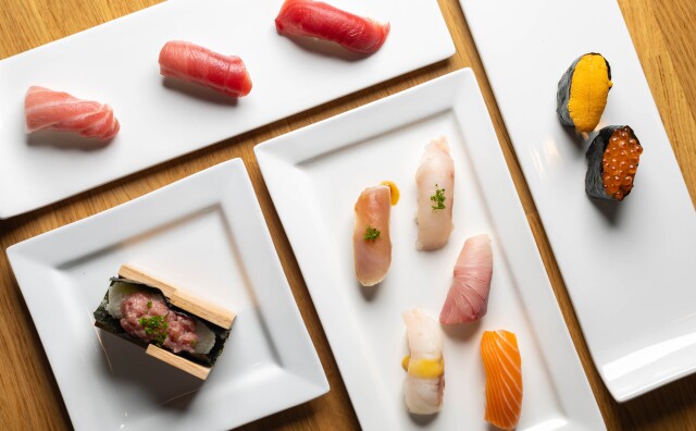 An overhead view of various white ceramic plates, both square and rectangular, each containing different types of sushi.