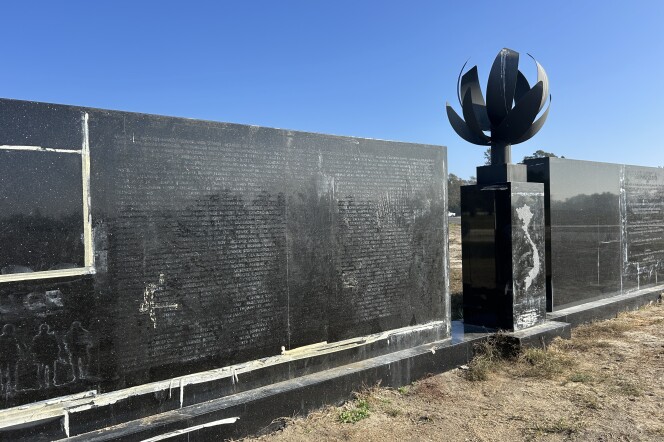 A diagonal view of a black granite wall with the outline of names vaguely visible on the surface and an internal flame in the center with a map of Vietnam engraved on it. 
