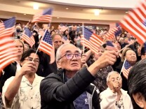 A crowd of mostly Asian Americans at a concert hall wave American flags.