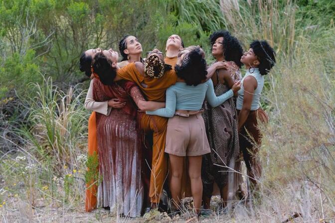 8 women in an embrace / huddle in a field looking up towards the sky