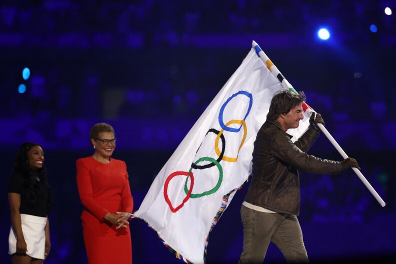 A man with light-tone skin walks with a flag away from two women, both with dark-tone skin. All are smiling.