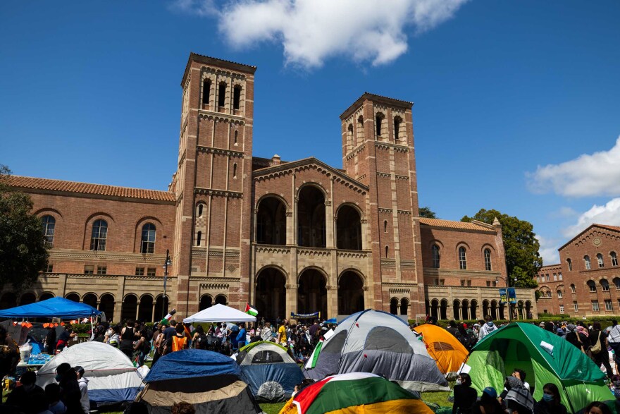 Various tents set up on a lawn in front of a large university brick building with arched windows and entrances.