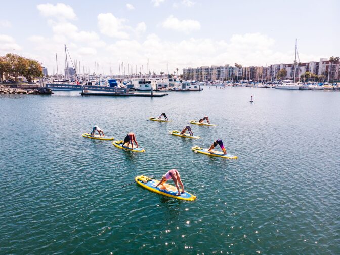 Seven people pratice yoga while standing on paddle boards in a marina.