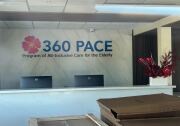 The interior of a business in transition — packing boxes are lined up, but there are welcoming flowers in the reception areas and computer monitors. Signage reads: "360 PACE Program of All-Inclusive Care for the Elderly"
