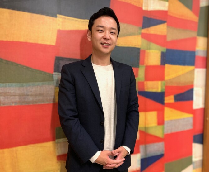 Photo of 35-year-old Korean American man in a blazer posing in front of a colorful office backdrop. .