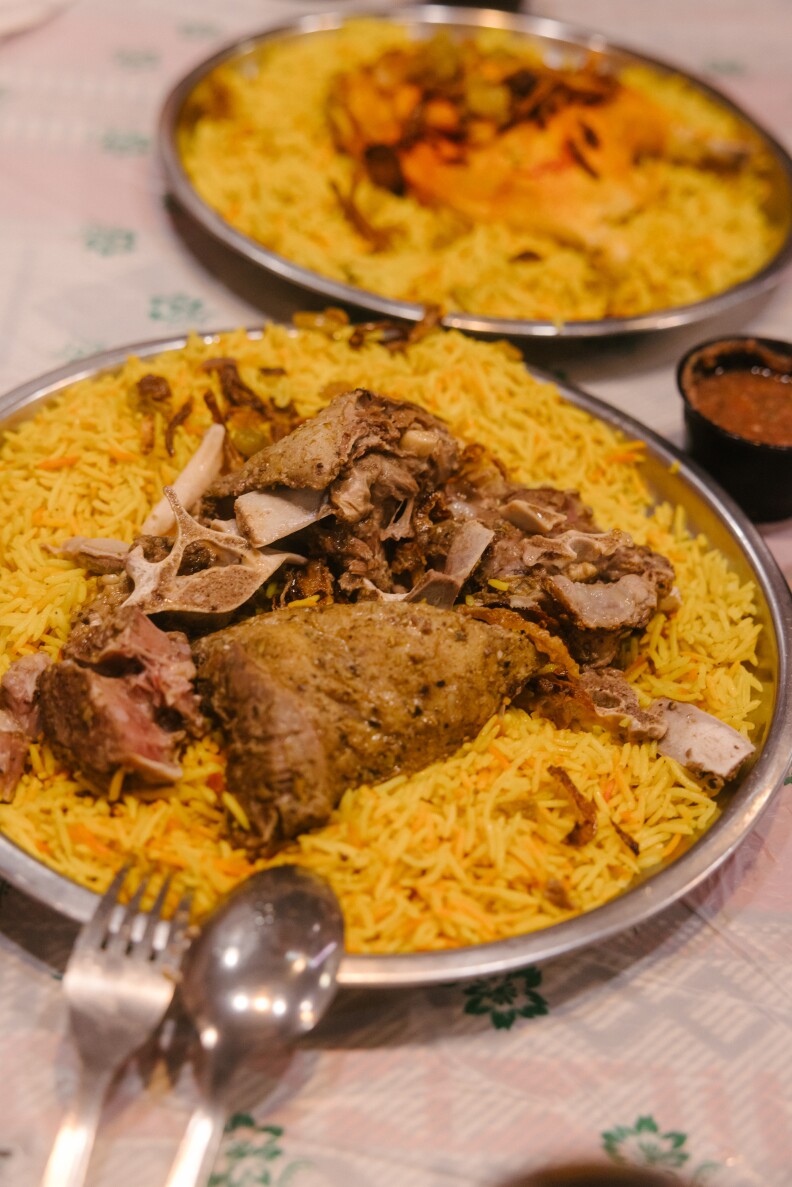 Two metal plates contain bright yellow rice with tender pieces of cooked chicken in the centers. A metal fork and spoon rests on one of them.