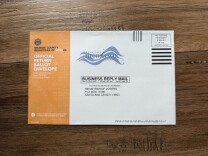 A close-up of a ballot return envelope from Orange County. The left side is orange and reads "Official Return Ballot Envelope."