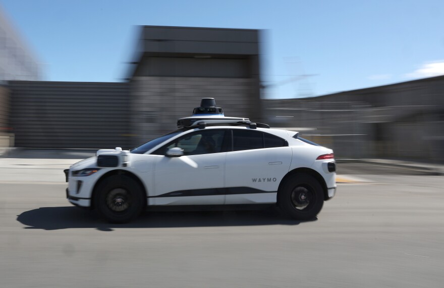 A white four-door sedan with a camera on top of it is zipping through a street