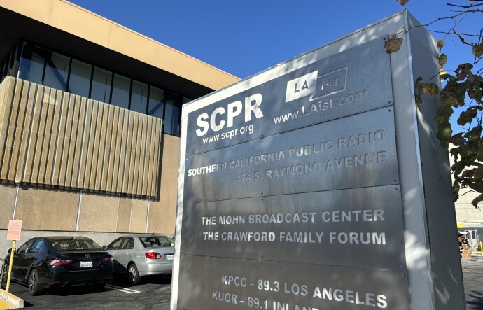 A metal sign outside a large beige building lists SCPR and LAist side-by-side.