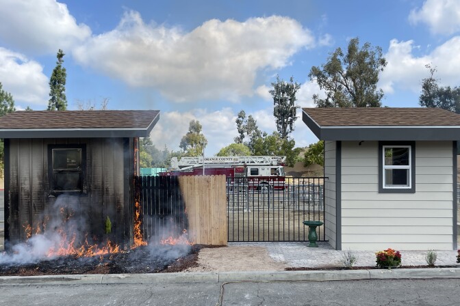 A small shed on fire on the left and one not burning on the right.
