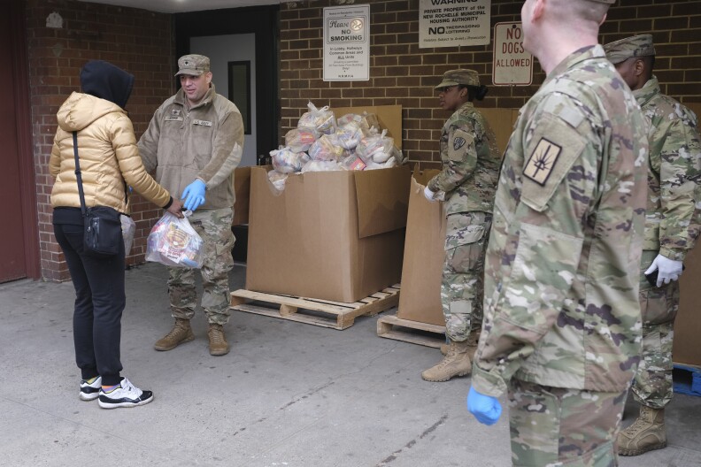 People in uniform hand out plastic bags full of supplies.