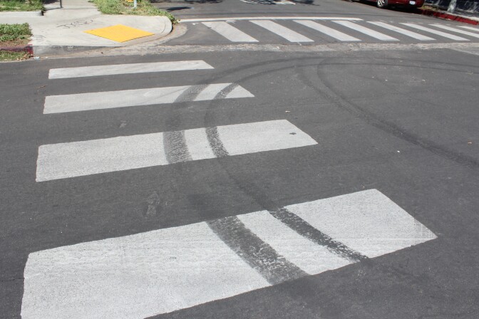 Circular tire marks cover over a portion of white paint from a crosswalk.