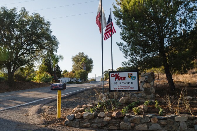 American and California flags fly next to the CalFire De Lus Station 16 sign. A mailbox on a post is painted with flames.