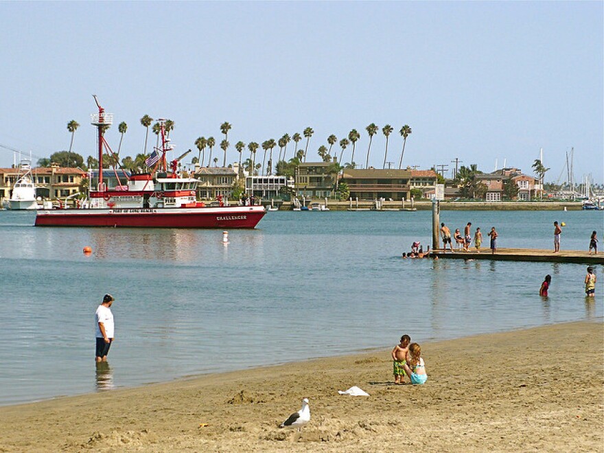 A person stands in the water while two kids play on the sand.