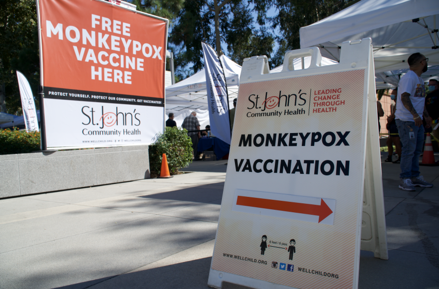 Signs point to where to line up to receive the mpox vaccine at DTLA Proud an LGBTQ+ festival.