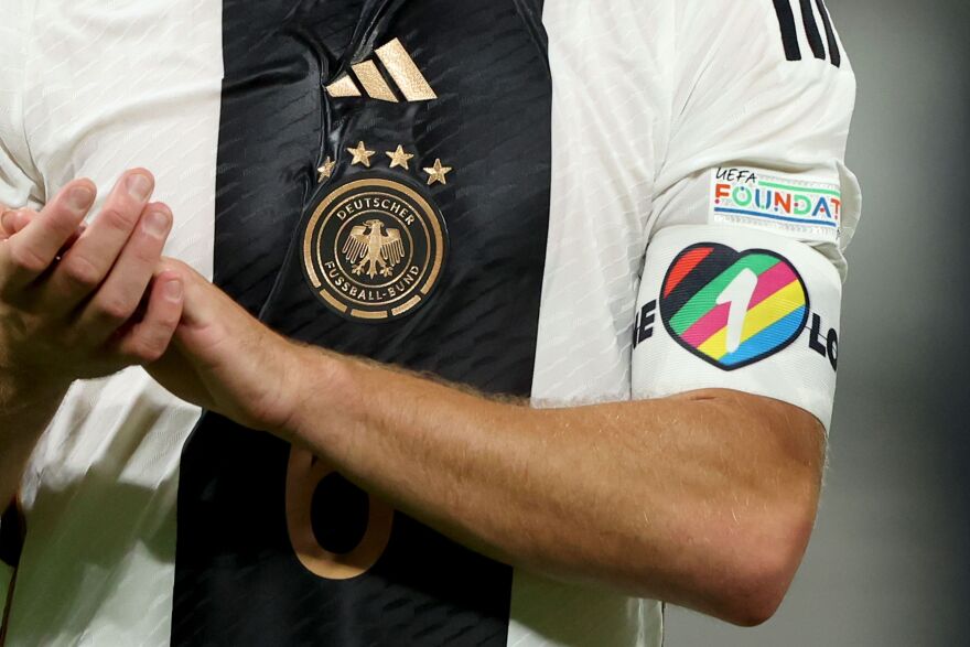 A heart armband on a player's uniform sleeve has rainbow-like colors.