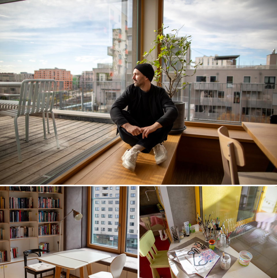 A man in a cap sits on a ledge next to a large window.