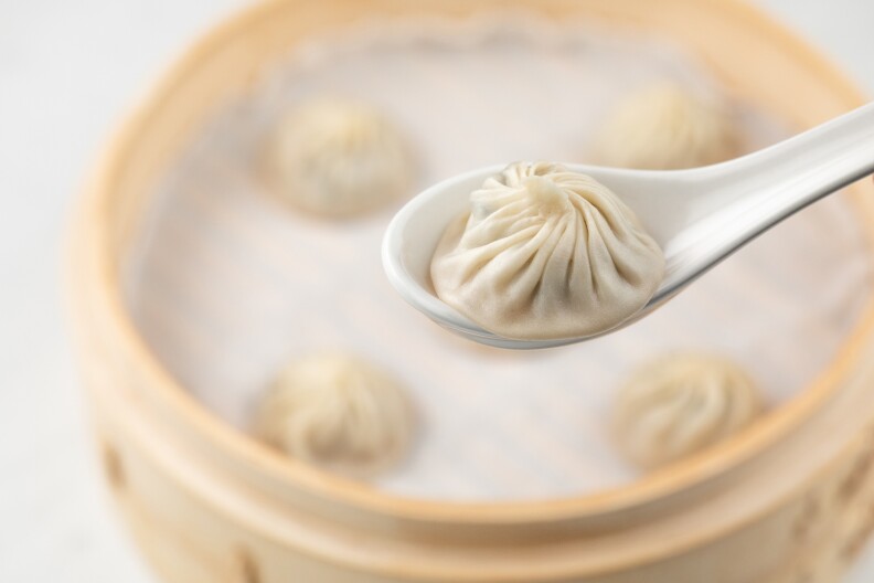 The mesmerizing pleats of a soup dumpling as it sits on the edge of a spoon, waiting to be devoured, are on great display here, with plenty more dumplings waiting patiently in the background.