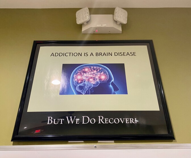 A picture inside a black frame hangs inside a room at the drug treatment facility where Jami is staying. It says addiction is a brain disease, but we do recover. There is a photo of a head with a brain in the middle.