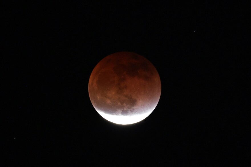 A full round moon is tinged red against the night sky.