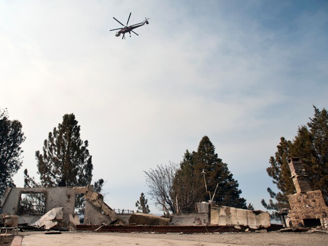 Helicopters carrying water fly over a Lake Hughes home that was destroyed. The fire continues to burn with 20 percent containment.