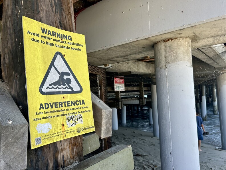 Pillars under a pier. A yellow sign is affixed to one.