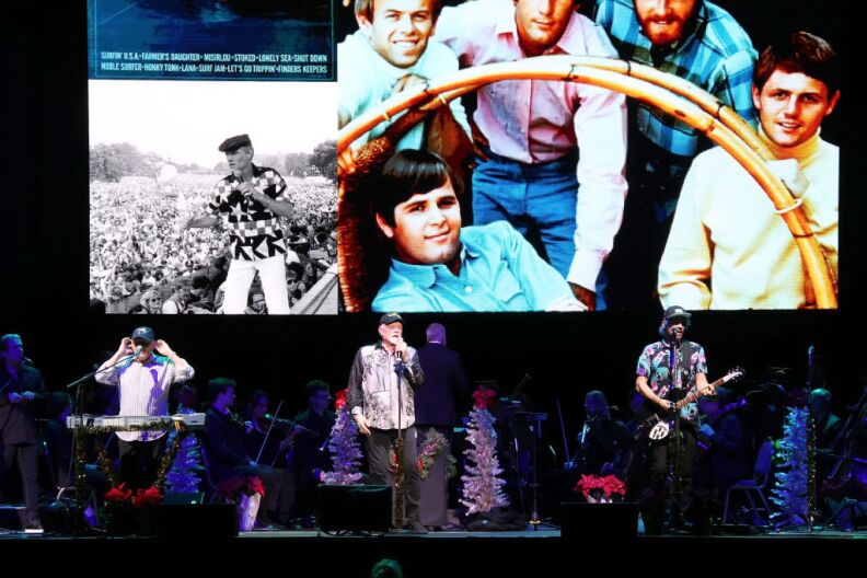 Band members perform on stage in front of large screen featuring images of their younger years.
