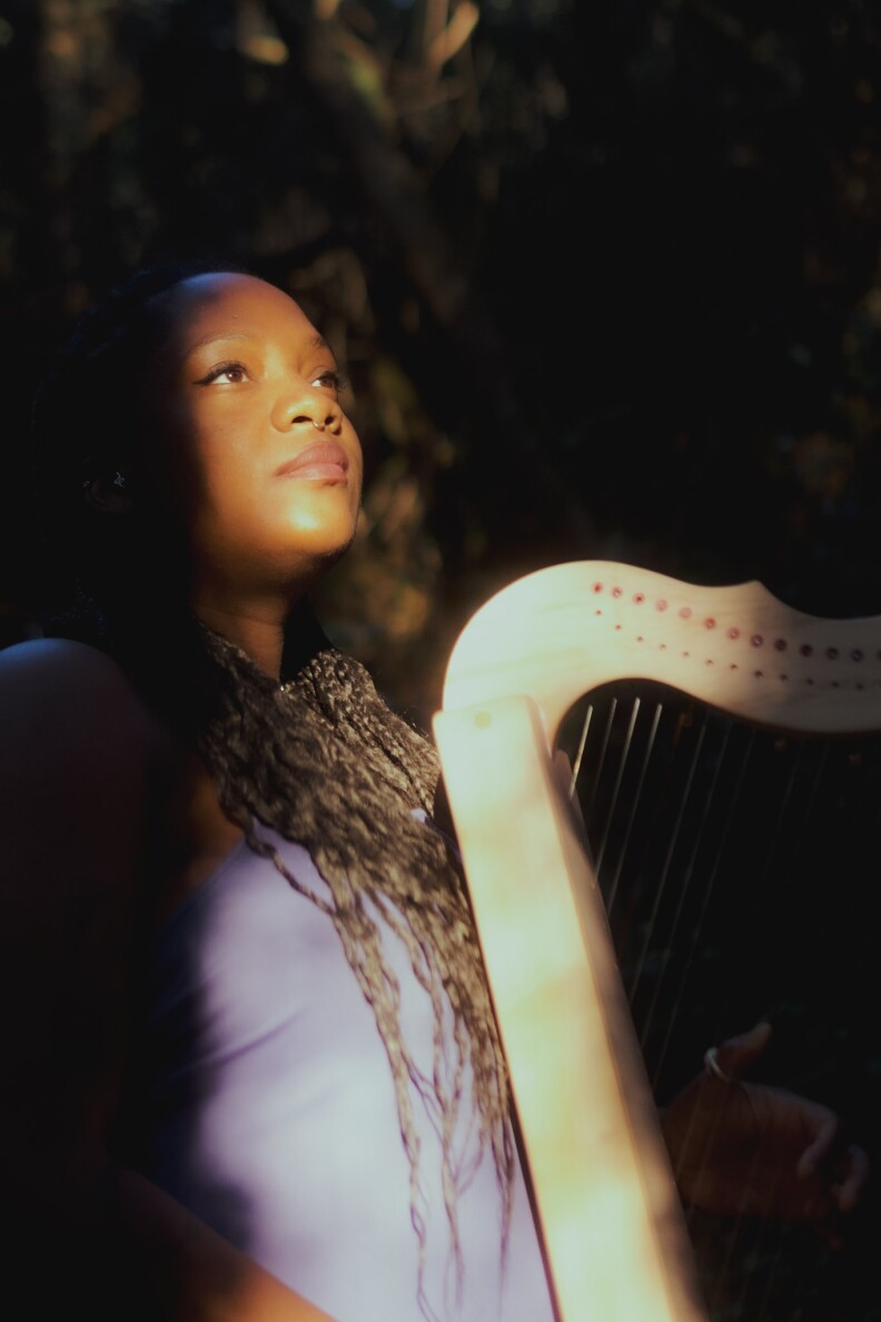 LA-based harpist Nailah Hunter sits at a harp. The sun is shining on her face. 