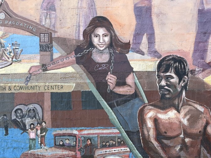 A mural depicts Filipino and Filipino American people and scenes from history. In the center of the photo is a portrait of Jake Zyrus in a black shirt before he came out as trans, next to boxer Manny Pacquiao. 