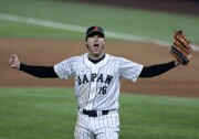 A baseball player wearing a pinstriped jersey that says Japan with the number 16 below it spreads his arms wide and shouts with joy