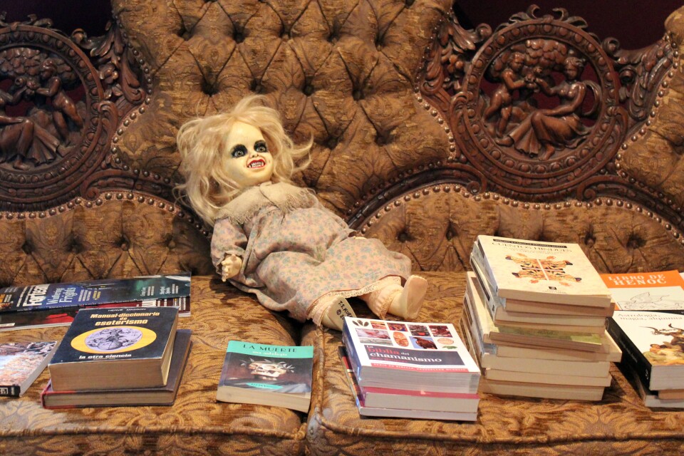 A couch piled with books and a demonic doll. 
